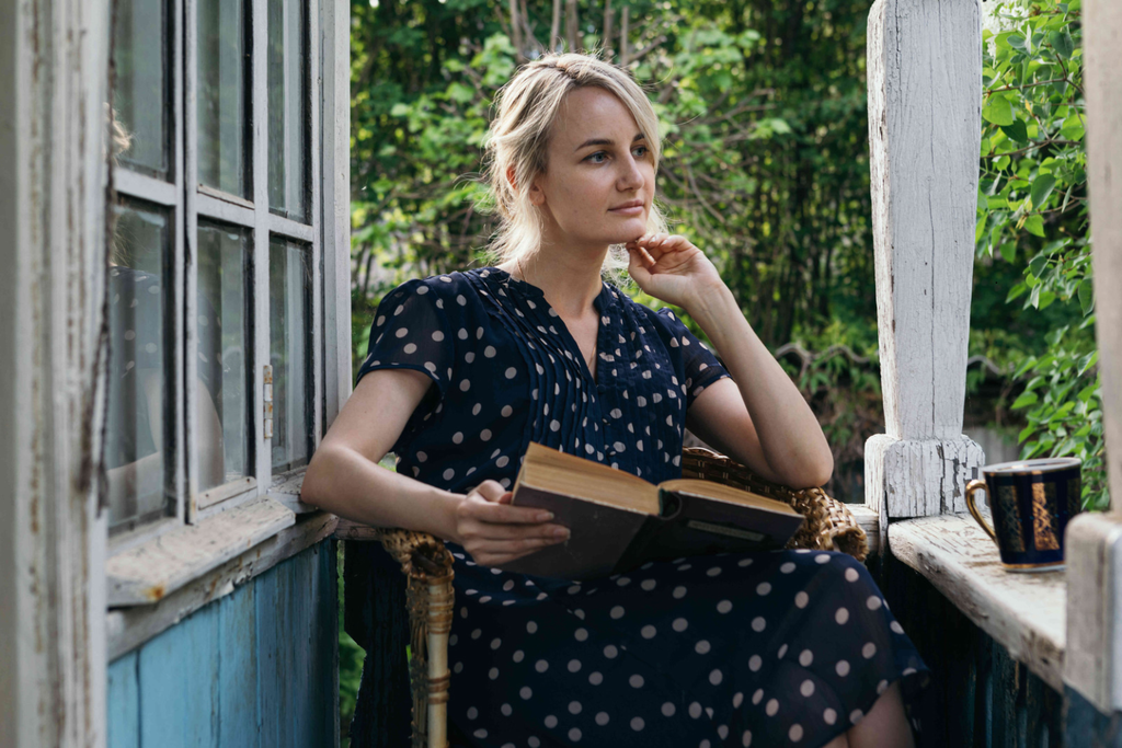 Person sitting on a porch step in morning light with a cup of coffee, pausing before the day