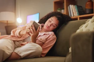Person sitting alone on a couch at night, lit by a phone screen showing a chatbot conversation
